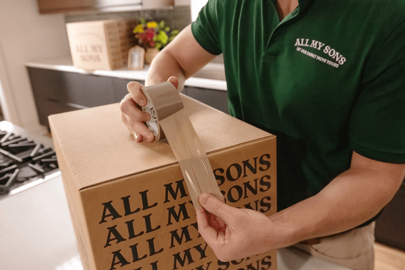 Movers from All My Sons Moving and Storage tape a box closed for a downsized move.