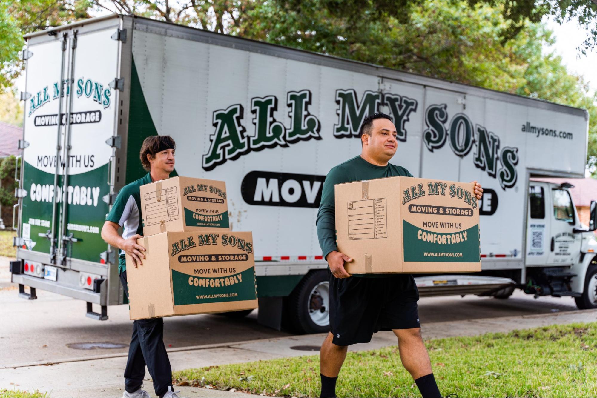 Two professional movers from All My Sons carry moving boxes away from a moving truck.