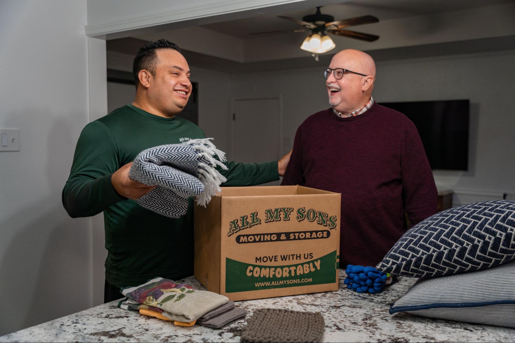 All My Sons professional packer puts a supportive hand on the customer's shoulder as he loads a box with blankets.